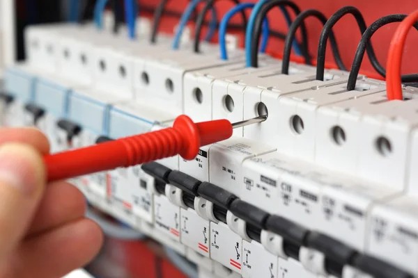 Pointe de touche d'un appareil de mesure posée sur les disjoncteurs d'un tableau électrique